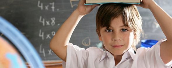 Child holding book on his head while standing in classroom