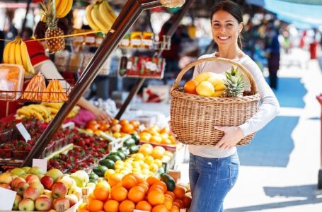 Woman holding basket of fruit in front of fruit stand.